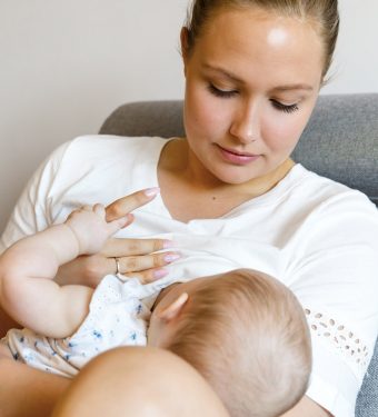 Caring young mother breastfeeds baby girl Portrait of a loving mother in sofa breastfeeding baby girl. Newborn child fed with breast milk by mom.